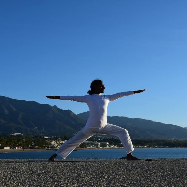 Silhouette of a person in a powerful yoga warrior pose against a sunrise.